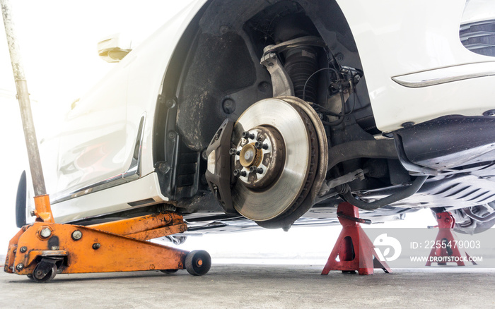 Car without wheel on car jack with car stands for safety in repair shop background.