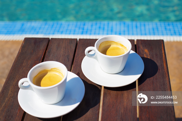 Two cups of coffee on the table near the pool.