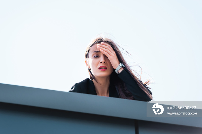 frightened businesswoman, suffering from acrophobia, looking down rooftop and covering face with han