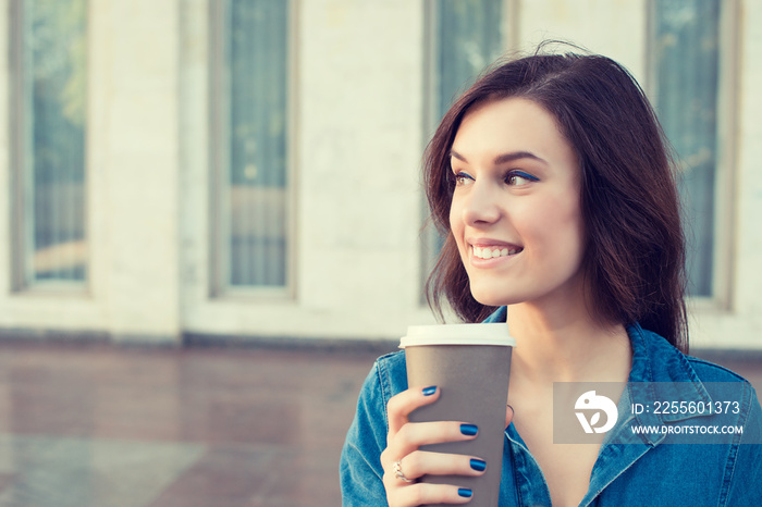 Smiling woman drinking coffee outdoors holding paper cup