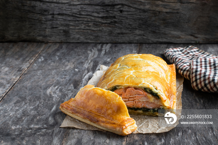 Homemade salmon wellington with spinach and mushrooms on rustic wooden table