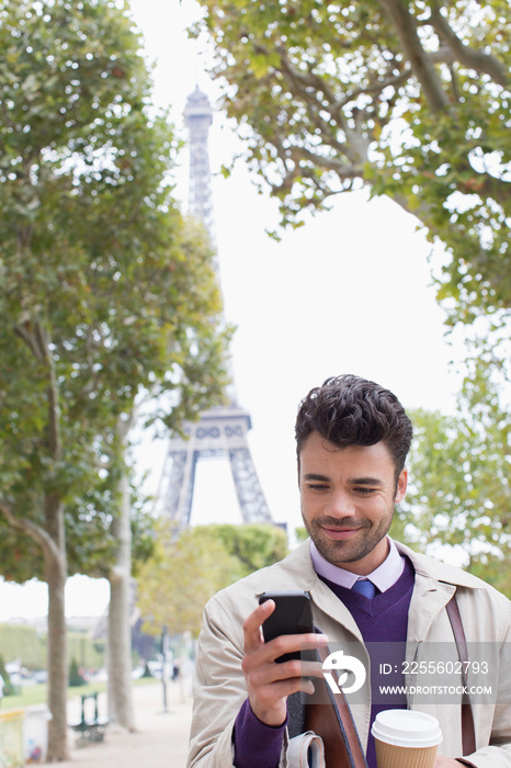 Businessman with coffee and smart phone below Eiffel Tower, Paris