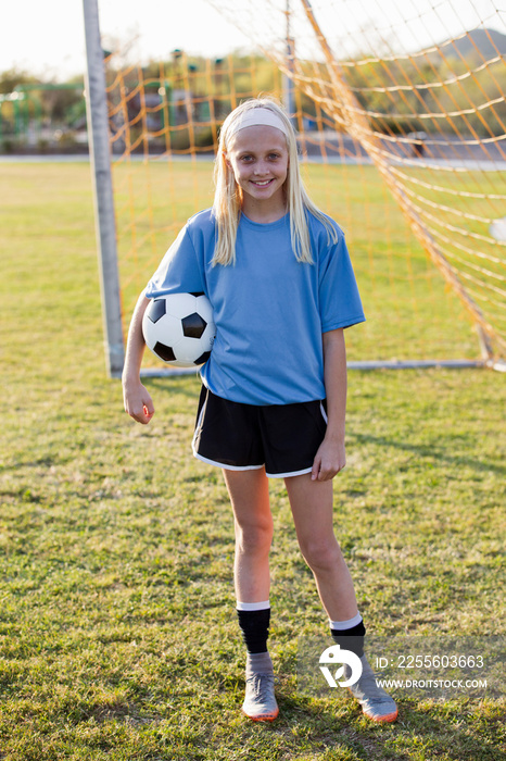 Portrait of smiling girl with soccer ball standing on grassy field