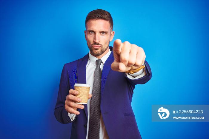 Young handsome business man drinking a coffee on a paper cup over blue isolated background pointing 