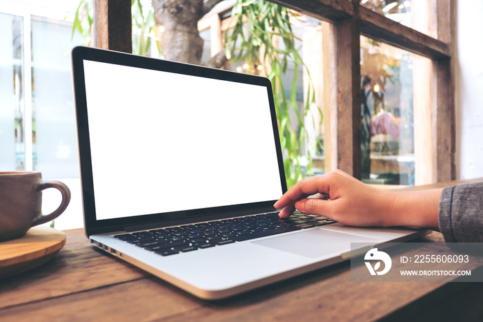 Mockup image of hand using laptop with blank white screen on vintage wooden table in cafe