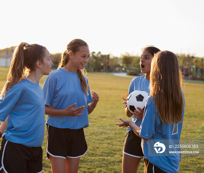 Girls talking while practicing with soccer ball on grassy field against clear sky during sunset