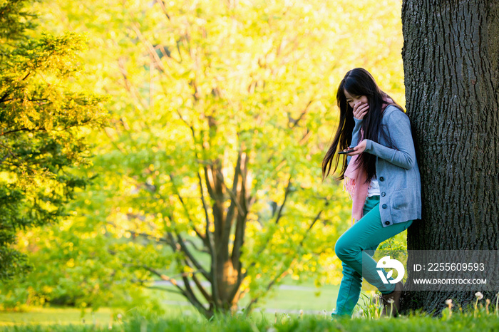 Young female laughing at mobile phone in park