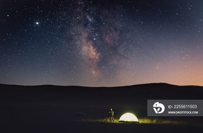 Couple stands by the tent with car in the background and looks to the stary sky. Travel joys and nig