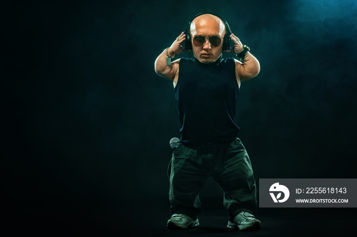 Portrait of stylish midget MC in with headphones and sunglasses posing with microphone.