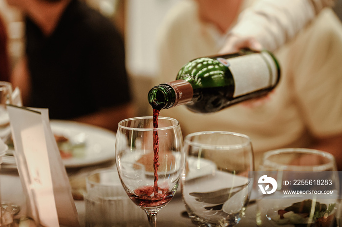 女服务员在餐厅的桌子上为品酒活动倒着装在玻璃杯里的红酒。模糊了
