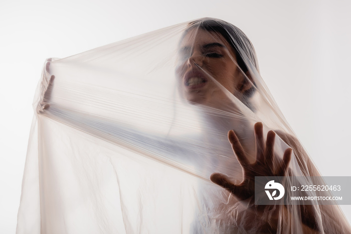 trapped and angry woman touching polyethylene isolated on white, ecology concept