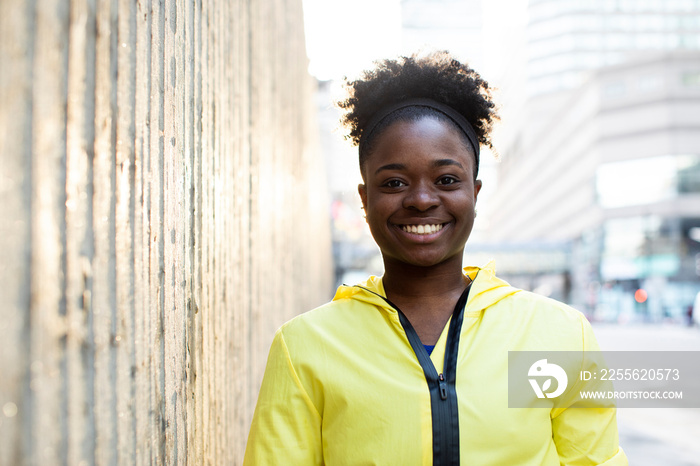 Portrait of smiling female athlete standing on sidewalk by wall in city