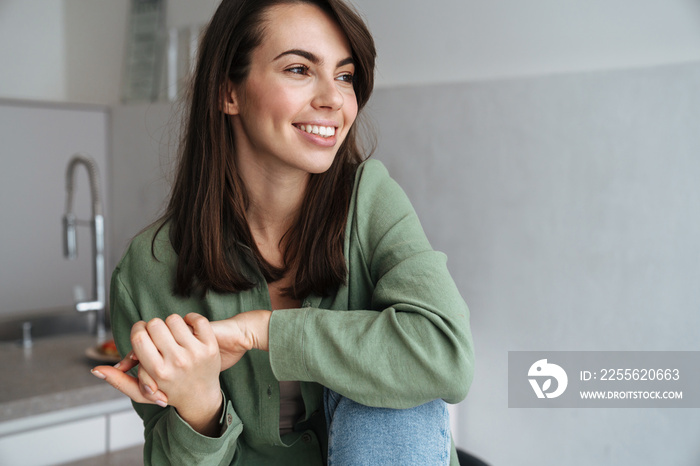 Young white woman smiling and looking aside while sitting at kitchen