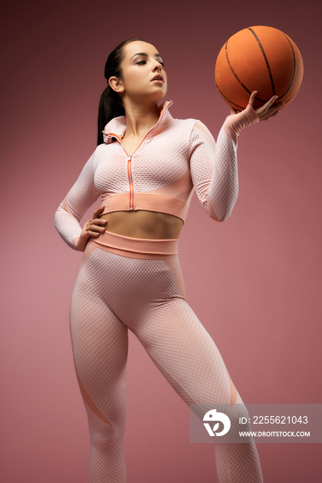 Beautiful young woman with basketball ball posing in studio