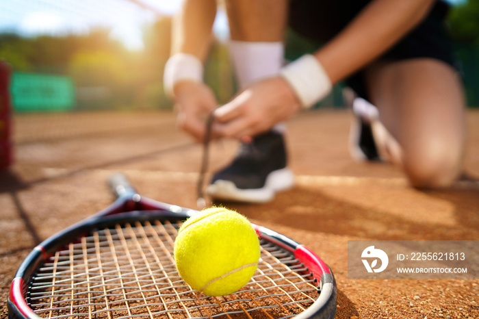 Tennis player tying his shoelaces. Selective focus on the ball and racket