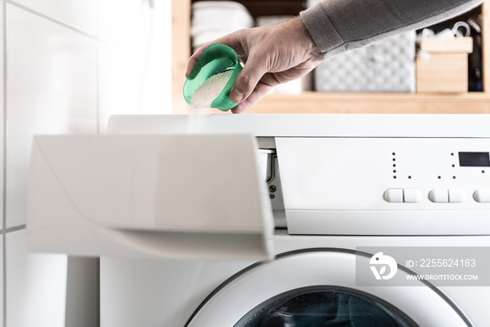 close-up of person using dosing aid to pout laundry detergent powder into washing machine