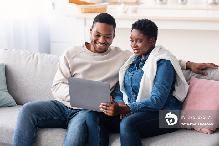 African american couple sitting on couch, using laptop