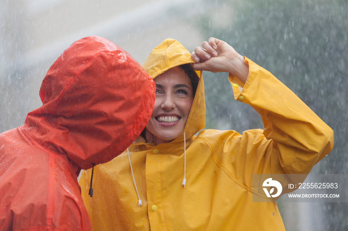 Happy young couple in raincoats standing in rain