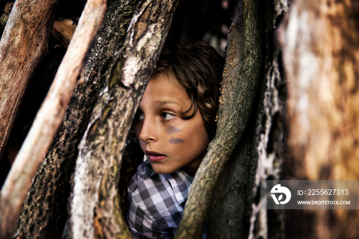 Close up of boy with painted face hiding behind wooden sticks