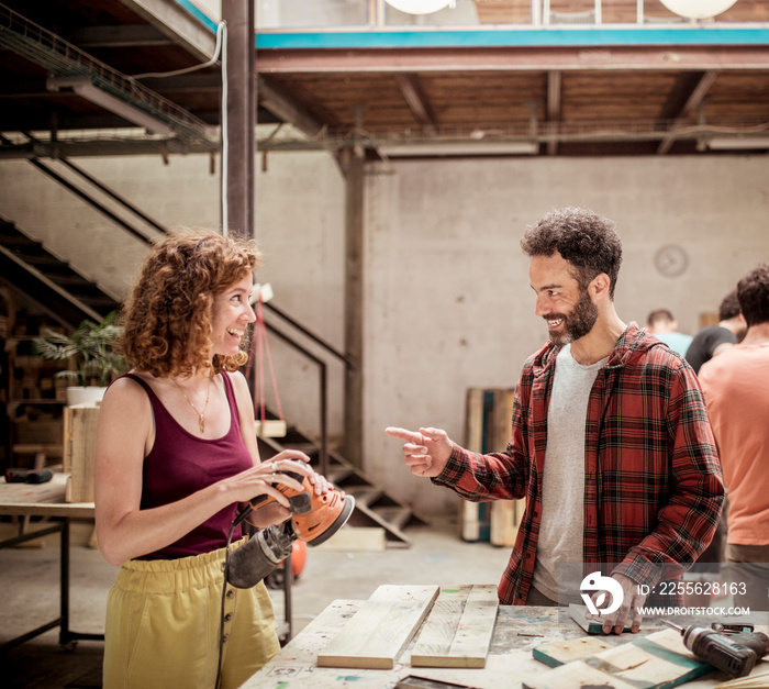 Smiling carpenters talking while working at workbench in workshop