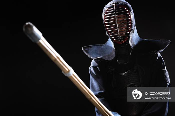 Kendo fighter in armor practicing with bamboo sword isolated on black