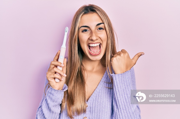 美丽的西班牙女人拿着电动牙刷，拇指向上，面带微笑，风趣幽默