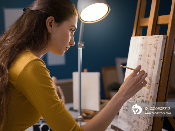 Beautiful young woman painting in the atelier