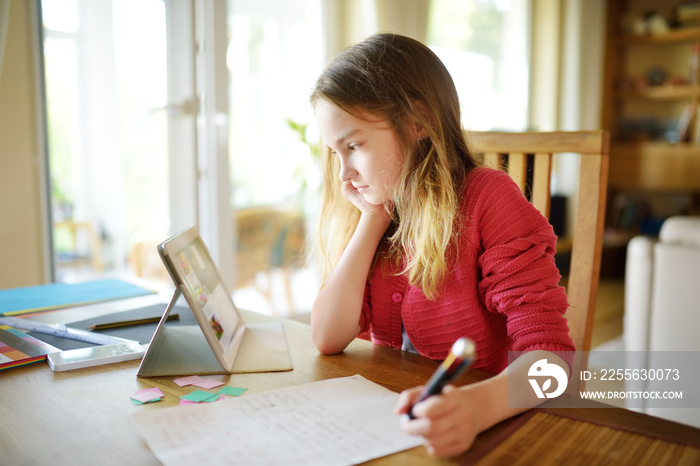 Smart preteen schoolgirl doing her homework with digital tablet at home. Child using gadgets to stud