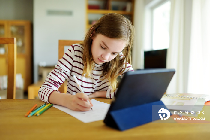 Smart preteen schoolgirl doing her homework with digital tablet at home. Education and distance lear