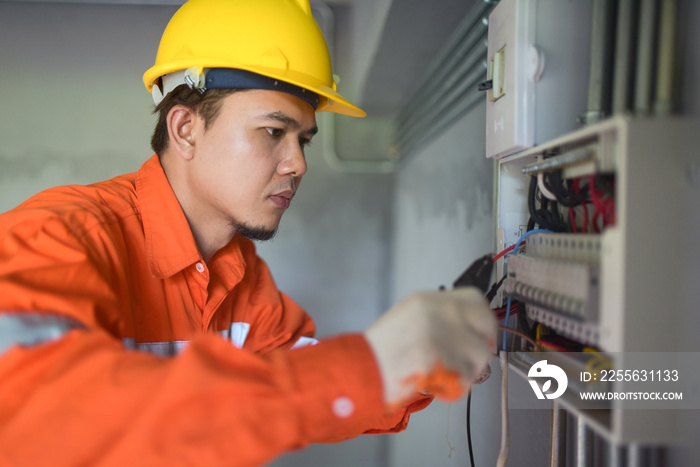 Side view of a handsome Asian electrician repairing an electrical box with pliers in the corridor.