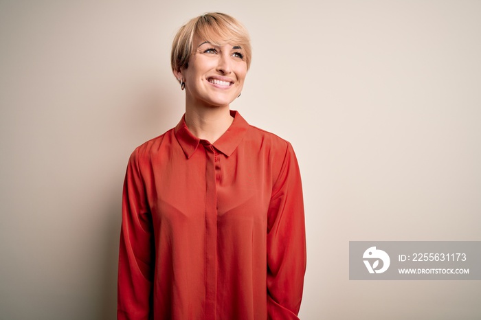 Young beautiful business blonde woman with short hair standing over isolated background looking away