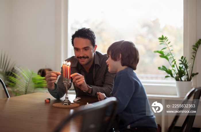 Boy looking at smiling father burning candles on menorah during Hanukkah festival