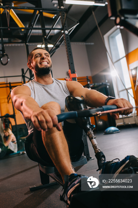 hardworking young sportsman with artificial leg working out with rowing machine at gym