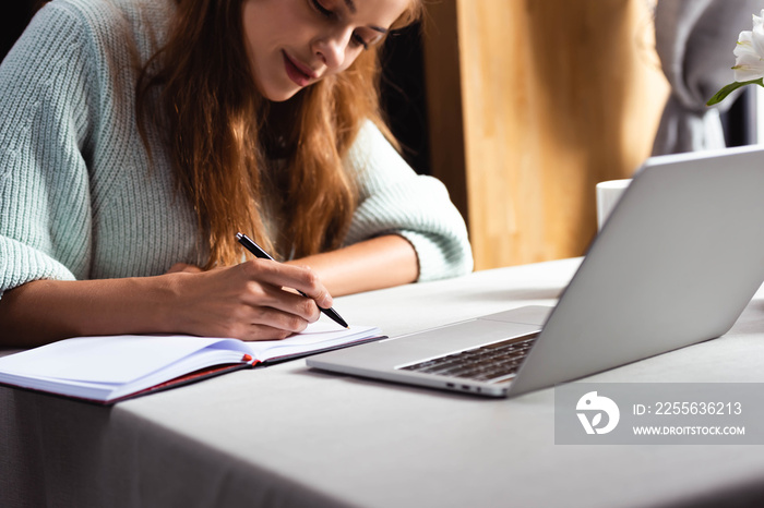 redhead woman writing and studying online with laptop in cafe