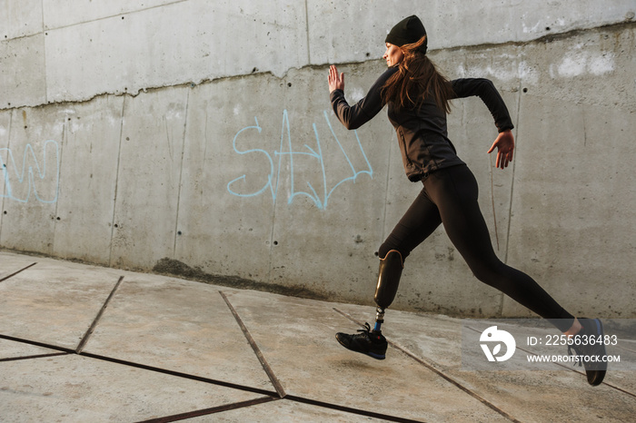 残疾女运动员的肖像，穿着运动服，假肢，沿着混凝土在户外跑步