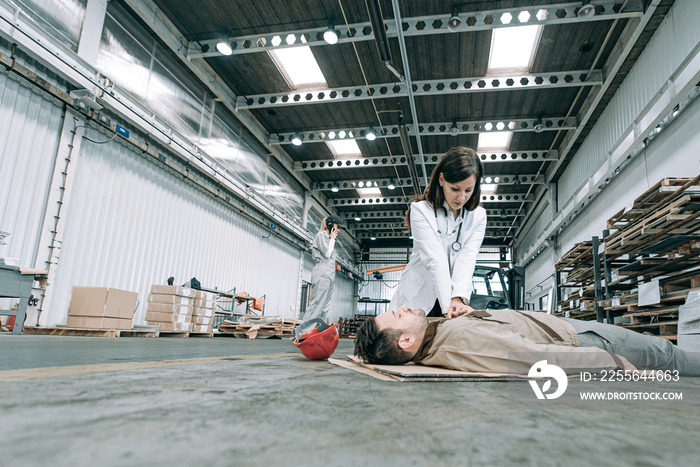 Female doctor resuscitate worker at factory hall.