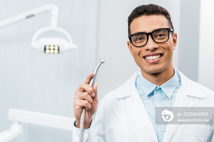 smiling african american dentist in glasses holding drill