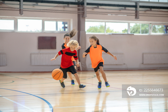 Kids in bright sportswear playing basketball together and running