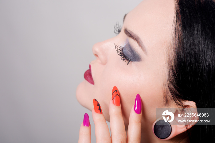 Portrait of a brunette girl. Halloween woman makeup, spider web on eyelashes. Red maniure on long na