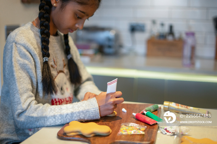 Girl decorating gingerbread cookies in kitchen