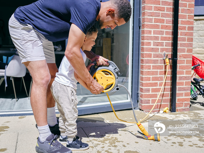 Father with son holding garden hose in back yard