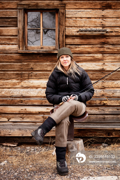 Woman sitting by house with fishing rod