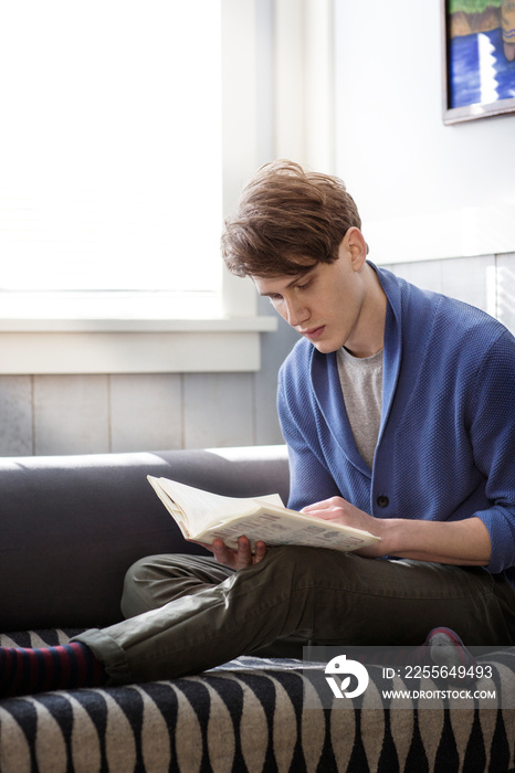 Young man reading book on sofa
