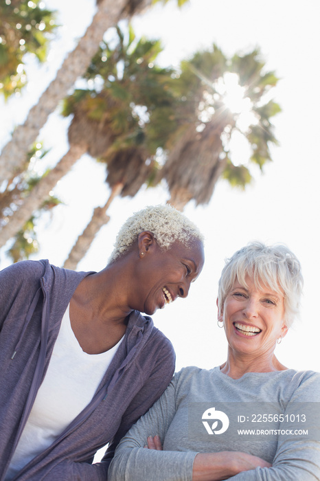 Happy senior women friends below sunny palm trees