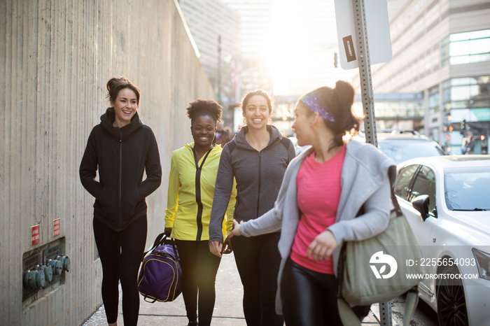 Happy female athletes talking while walking on sidewalk in city