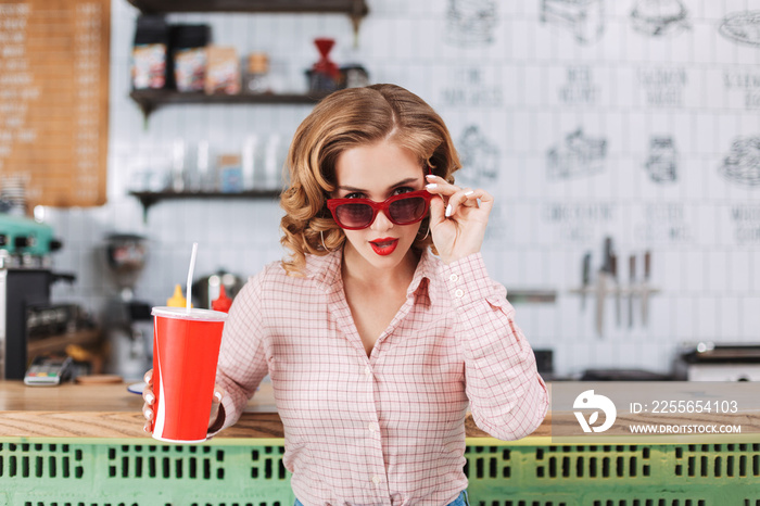 Portrait of beautiful lady in sunglasses sitting at the bar counter with soda water in hand and drea