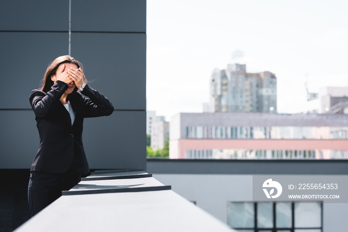 young businesswoman, suffering from fear of heights, standing on rooftop and covering face with hand