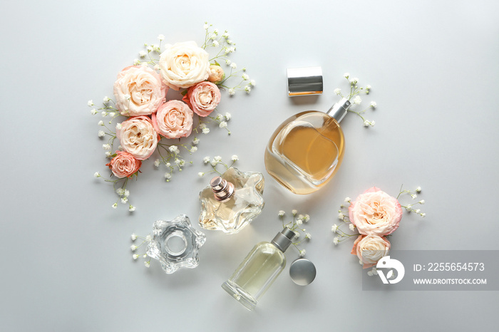 Bottles of perfume and flowers on light background