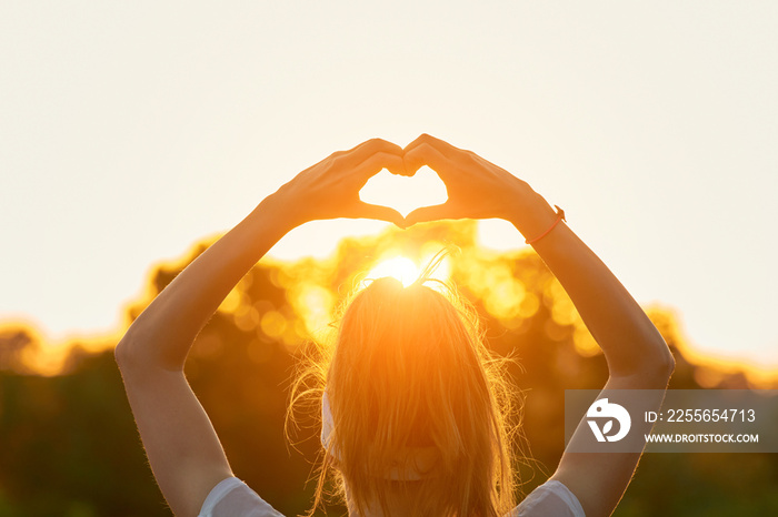 Woman in nature holding heart-shape symbol made with hands.