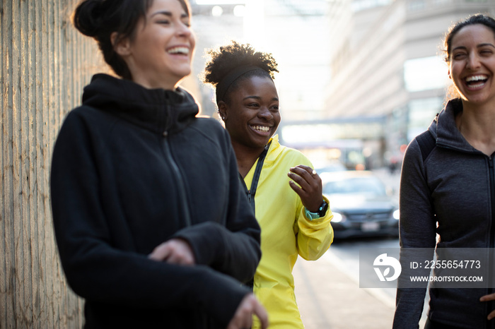 Happy female athletes talking while standing on sidewalk in city